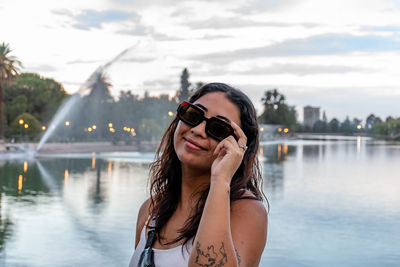 Portrait of young woman taking selfie while standing against lake