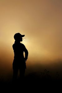 Silhouette of woman standing on field against cloudy sky during sunruse