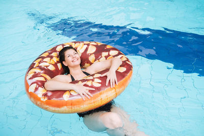 Happy young woman plus size body positive in inflatable doughnut circle swimming in the pool