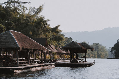 Stilt house by trees and buildings against sky