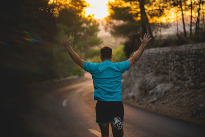 Rear view of man with arms outstretched standing at sunset