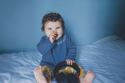 Smiling cute girl playing with headphones while sitting on bed at home