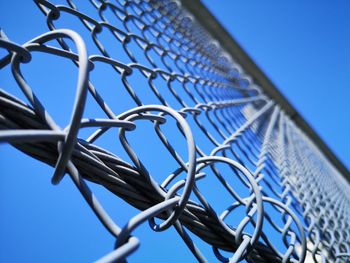 Low angle view of chainlink fence against clear blue sky