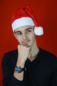 Thoughtful man wearing santa hat looking away against red background