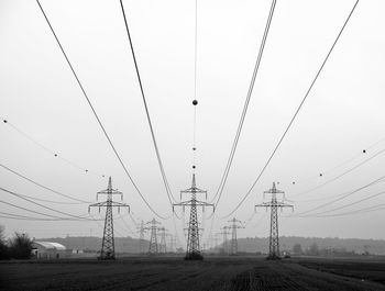 Electricity pylons on field against clear sky