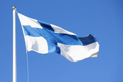 The flag of finland waves in the wind against the blue summer sky