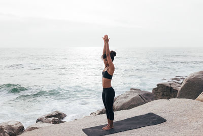 Full length of woman doing yoga on beach against sky