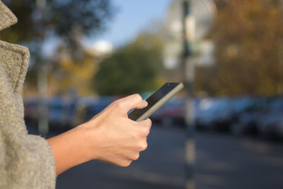 Cropped image of woman using mobile phone in city