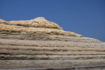 Low angle view of rocky mountain against clear blue sky