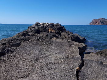 Rock on beach against clear blue sky