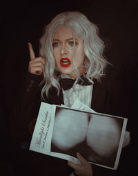 Angry young woman holding photograph against black background
