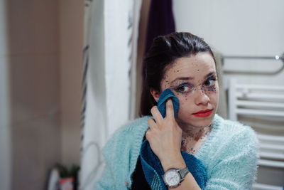 Woman removing glitter from face with towel in bathroom