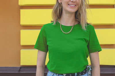Portrait of a smiling young woman standing against yellow wall