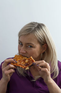 Close-up portrait of mature woman eating pizza against gray background