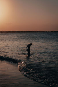 Silhouette woman walking at beach against sky during sunset