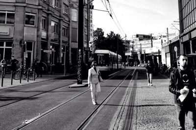 People walking on railroad track in city against clear sky