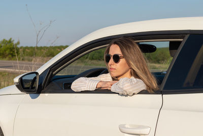 Young girl in sunglasses enjoying the views from a white car window in golden hour spring time