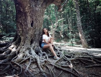 Full length portrait of young woman sitting at forest