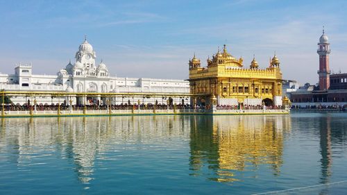 Golden temple by river against sky in city