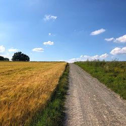 Dirt road amidst field against sky