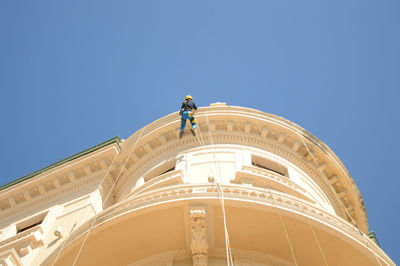 Low angle view of worker on rope while working at building