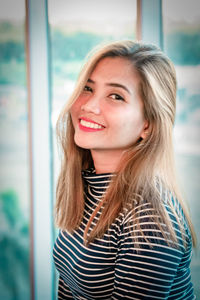 Portrait of smiling young woman against glass window