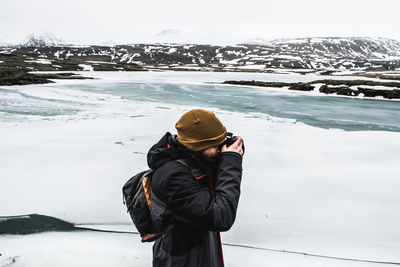 Man standing on snow covered shore against snowcapped mountains