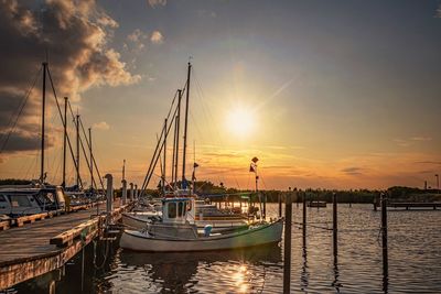 Sailboats moored in harbor at sunset