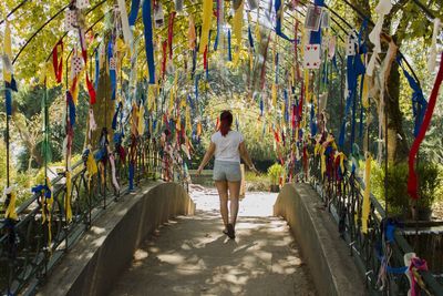 Rear view full length of woman amidst colorful ribbon decorations on footbridge