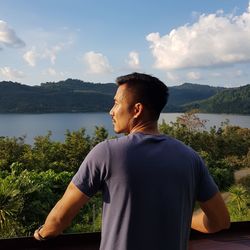 Young man looking at lake against sky