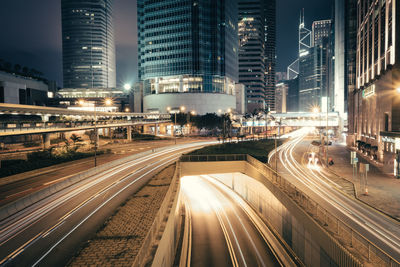 Light trails on city street by illuminated buildings at night