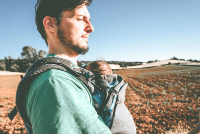 Portrait of young man looking away on field against sky