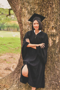 Portrait of young woman with arms crossed standing by tree at park