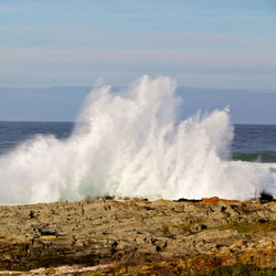 Waves splashing on shore against sky