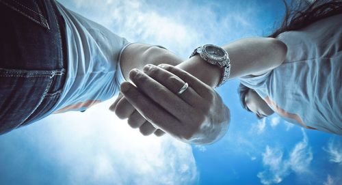 Low angle view of woman holding hands against blue sky