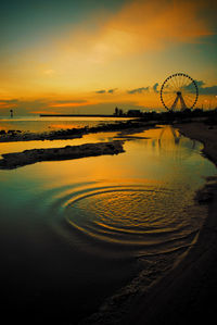 Silhouette ferris wheel at beach against sky during sunset