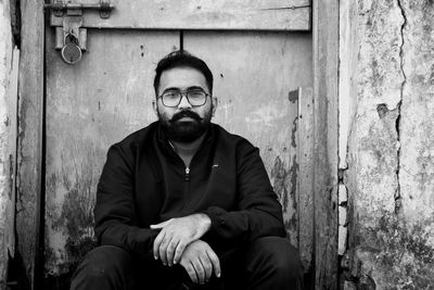 Portrait of young man sitting against wall