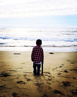 Rear view of boy standing on beach against sky