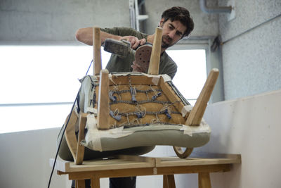 Low angle view of a man repairing and restoring an old chair