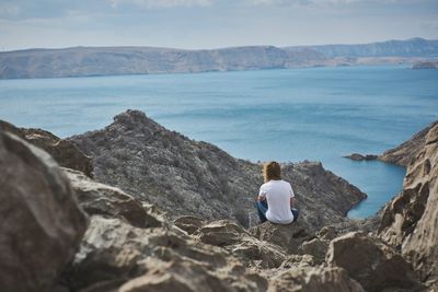 Rear view of young man sitting on rocky shore