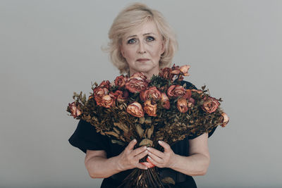 Portrait of woman holding flowers against gray background