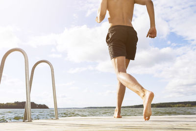 Low section of man running on boardwalk at lake