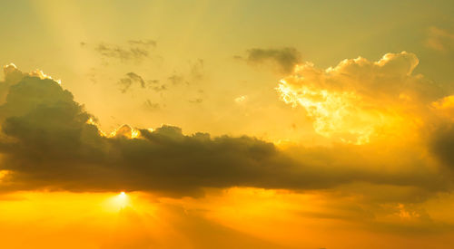 Low angle view of sunlight streaming through clouds during sunset