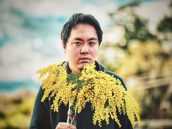 Portrait of young man standing on yellow flowering plant