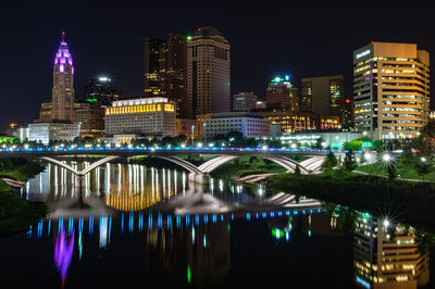 Illuminated bridge over river by buildings against sky at night