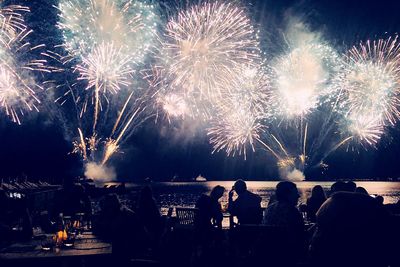 Silhouette people sitting in cafe by firework display over river at night