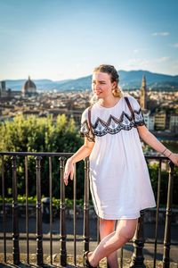 Young woman standing by railing against sky