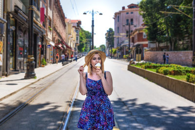 Portrait of smiling young woman eating ice cream on road in city