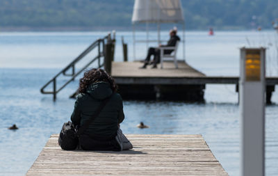Rear view of woman sitting on jetty over lake against sky