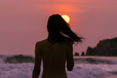 Rear view of woman standing against sea during sunset